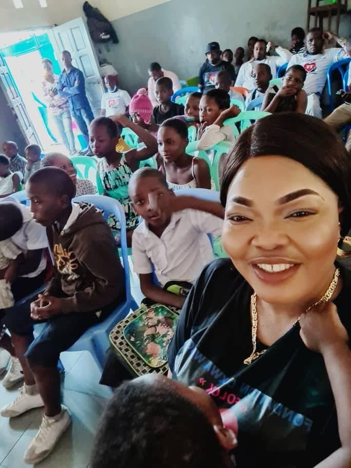 Une membre de la FOLOK souriante au milieu d'enfants assis dans une salle
